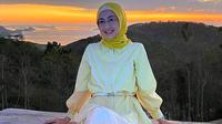 Menikmati sunset di NTT, Desy tampil stylish dengan padu padan striped blouse, rok, dan hijab kuning.