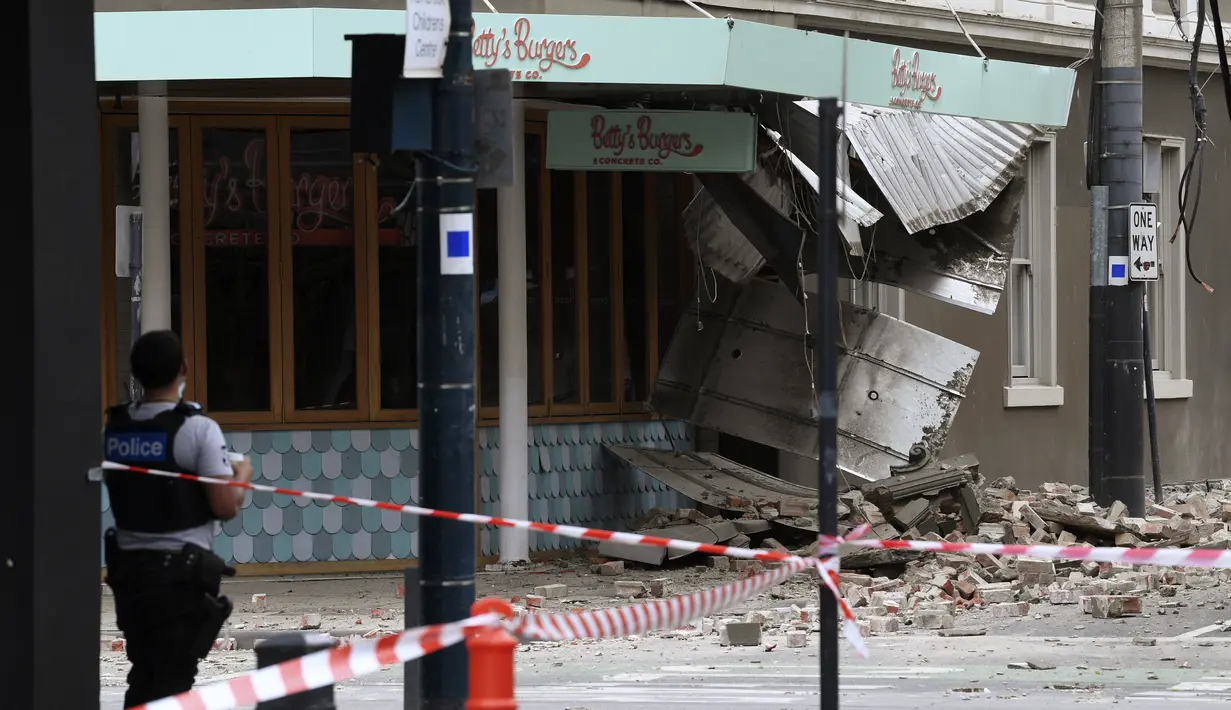 Seorang petugas polisi menutup persimpangan di mana puing-puing berserakan di jalan setelah gempa merusak sebuah bangunan di Melbourne, Rabu (22/9/2021). Gempa magnitudo 5,8 melanda dekat Melbourne dan guncangannya terasa di sejumlah wilayah di Australia pada Rabu pagi. (James Ross/AAP Image via AP)