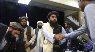Juru bicara Taliban Zabihullah Mujahid, berjabat tangan dengan seorang wartawan setelah konferensi pers pertamanya, di Kabul, Afghanistan, pada Selasa (17/8/2021). Selama bertahun-tahun, Mujahid adalah sosok misterius yang mengeluarkan pernyataan atas nama para militan. (AP Photo/Rahmat Gul)