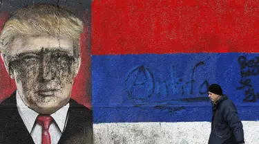 Seorang pria melintas di depan grafiti bergambar Presiden AS terpilih Donald Trump yang dirusak dengan cat di Belgrade, Serbia, Jumat (20/1). Trump hari ini akan dilantik menjadi Presiden AS. (AP Photo / Darko Vojinovic) 