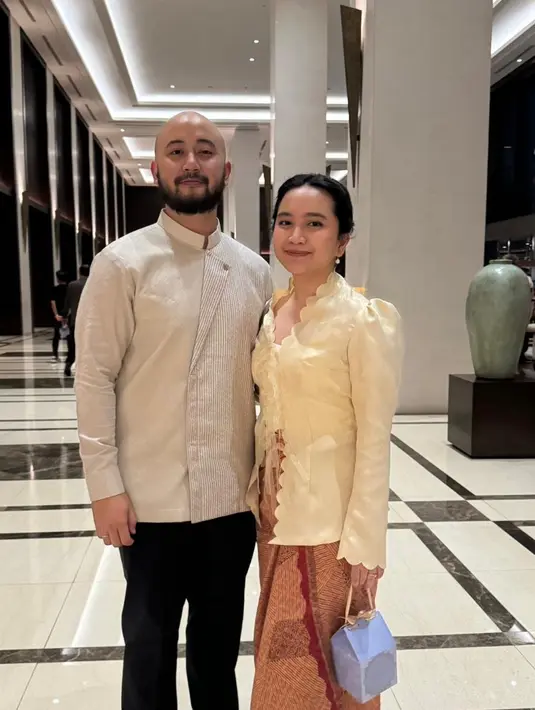 Rachel Amanda tampil anggun kenakan dress warna kuning dengan sentuhan vintage yang terlihat pada detail puff di lengan. Ia hadir bersama suaminya yang mengenakan top bersiluet surjan warna putih. [@auroraamanda95].
