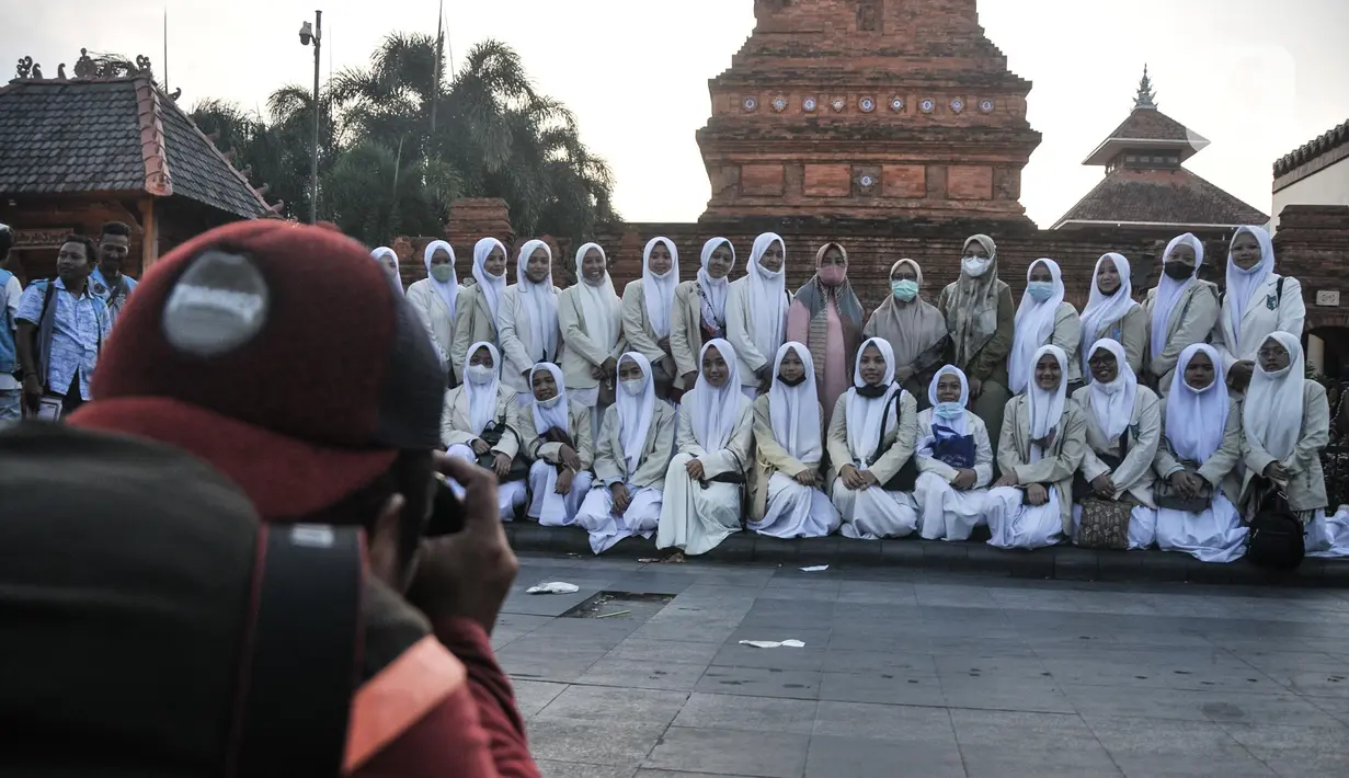 Fotografer saat memotret peziarah dengan latar belakang Menara Kudus, Kauman, Kabupaten Kudus, Jawa Tengah, Rabu (30/3/2022). Musim ziarah membawa berkah tersendiri bagi para fotografer keliling di kawasan Makam Sunan Kudus. (merdeka.com/Iqbal S. Nugroho)