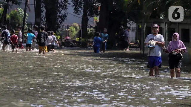 Warga melintasi genangan air yang merendam jalan di kawasan Kampung Makasar, Jakarta Timur, Senin (7/7/2025). (Liputan6.com/Herman Zakharia)