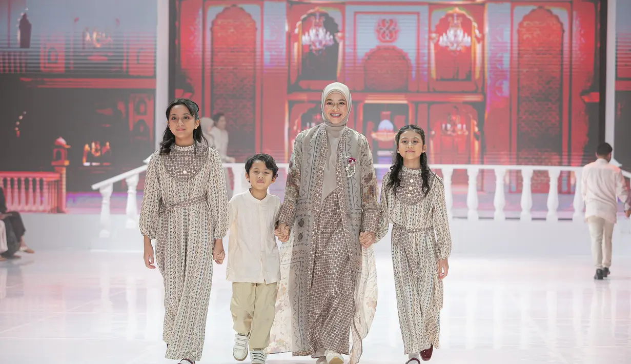 Natasha Rizky tampil penuh kehangatan saat melangkah di runway bersama ketiga buah hatinya, yang dikenal sebagai Trio Strong, dalam balutan busana serasi bernuansa krem dan cokelat lembut. Natasha mengenakan inner dress bermotif kecil bernuansa earthy yang jatuh lurus dan ringan, lalu dilapis dengan outer panjang berpotongan clean yang menghadirkan efek flowy saat ia berjalan. Ketiga anaknya tampil kompak dalam busana bermotif serupa, dengan potongan yang disesuaikan untuk anak-anak yang ringkas, nyaman, dan tetap terlihat rapi.  [Dok/Shi by Shireen & Zaskia Sungkar].