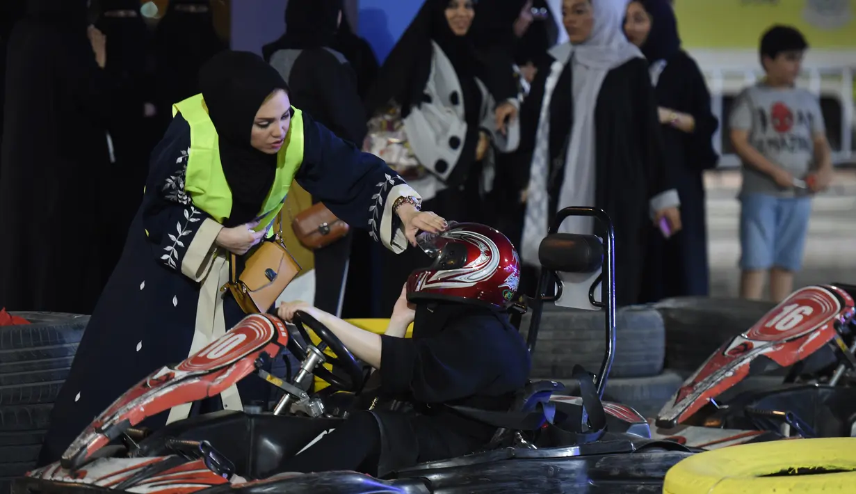 Petugas membantu memakaikan helm kepada wanita sebelum mencoba gokart selama workshop di Ibu Kota Riyadh, Arab Saudi, Kamis (21/6). Pemerintah Arab Saudi kini telah memperbolehkan kaum wanita untuk mengendarai kendaraan. (FAYEZ NURELDINE/AFP)