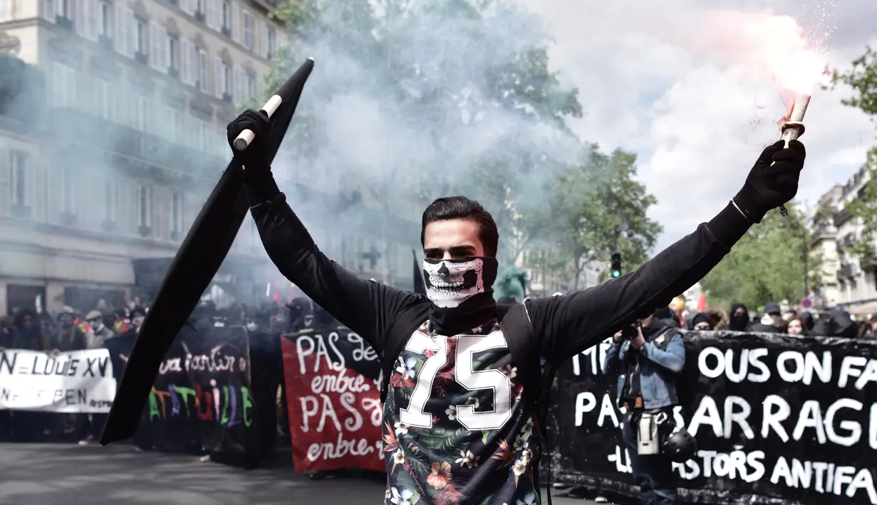 Seorang pria memegang bendera sambil manyalakan suar asap saat demonstrasi perayaan May Day di Paris, Prancis,Senin (1/5). Hari Buruh Internasional atau May Day di Paris, diwarnai bentrokan antara pengunjuk rasa dengan polisi.  (PHILIPPE LOPEZ/AFP)