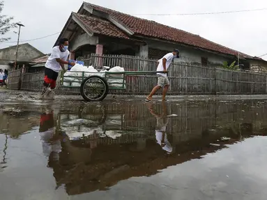 Jurnalis membawa gerobak berisi bantuan sembako di Pulau Panjang, Serang, Banten, Sabtu (30/1/2021). Perwakilan wartawan yang tergabung dalam Jurnalis Peduli menyalurkan bantuan sembako dan uang tunai bagi warga terdampak Covid-19. (Liputan6.com/Pool/JP)