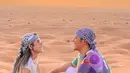 Foto pertama yang diunggah Via Vallen dan Chevra Yolandi menampilkan mereka duduk di padang pasir saling berhadapan. Keduanya tersiram cahaya jingga sang surya. Pasangan yang menikah pada 15 Juli 2022 ini kompak pakai celana warna gandaria. Bedanya, Chevra memadukannya dengan kaus motif abstrak warna-wanir. Via pakai atasan putih polos. (Foto: Dok. Instagram @viavallen)