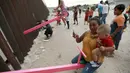 Seorang ibu dan bayinya bermain jungkat-jungkit yang dipasang di antara pagar pemisah Meksiko dengan Amerika Serikat, Ciudad de Juarez, Meksiko, Minggu (28/7/2019). Jungkat-jungkit tersebut dirancang seorang profesor arsitektur California, Ronald Rael. (AP Photo/Christian Chavez)