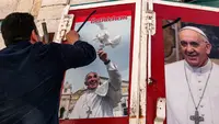 Seorang pria menempelkan foto mendiang Paus Fransiskus di luar sebuah toko di kota alkitabiah Betlehem di Tepi Barat yang diduduki Israel pada 21 April 2025. (HAZEM BADER/AFP)