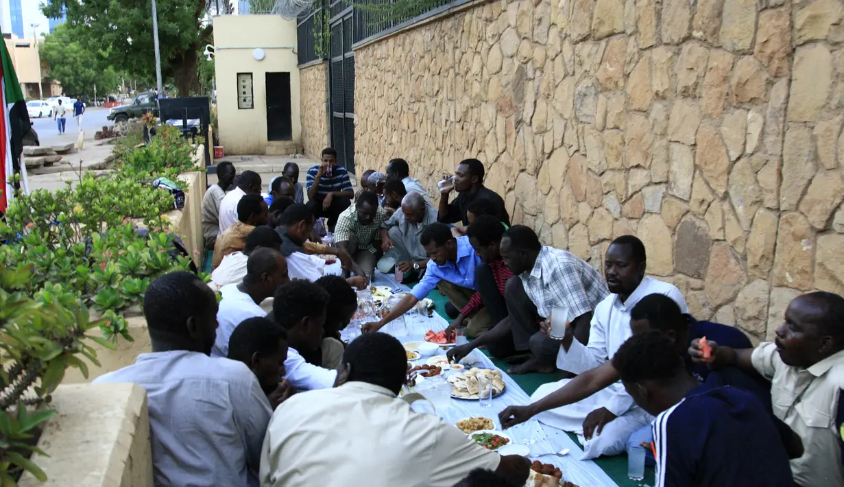 Sejumlah pria Sudan menikmati makanan buka puasa selama bulan suci Ramadan di depan kedubes Inggris di ibukota Khartoum (23/5/2019). Duta Besar Inggris untuk Sudan, Irfan Sidiq menggelar buka puasa bersama di ibu kota tersebut. (AFP Photo/Ebrahim Hamid)