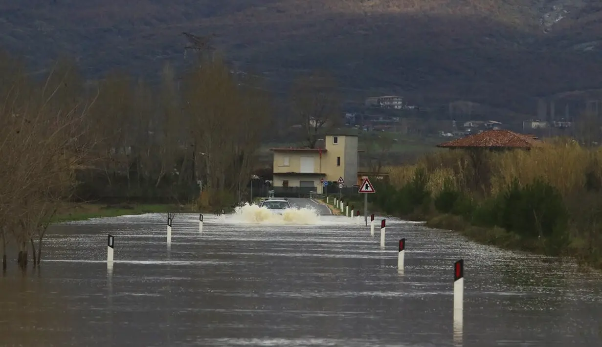 Seorang pengemudi mencoba menyeberangi jalan yang banjir setelah hujan lebat di Desa Obot, sekitar 100 kilometer (60 mil) barat laut Tirana, Albania, Senin (11/1/2021). Hujan deras dan salju selama beberapa hari terakhir telah membanjiri banyak kawasan di Albania. (AP Photo/Hektor Pustina)