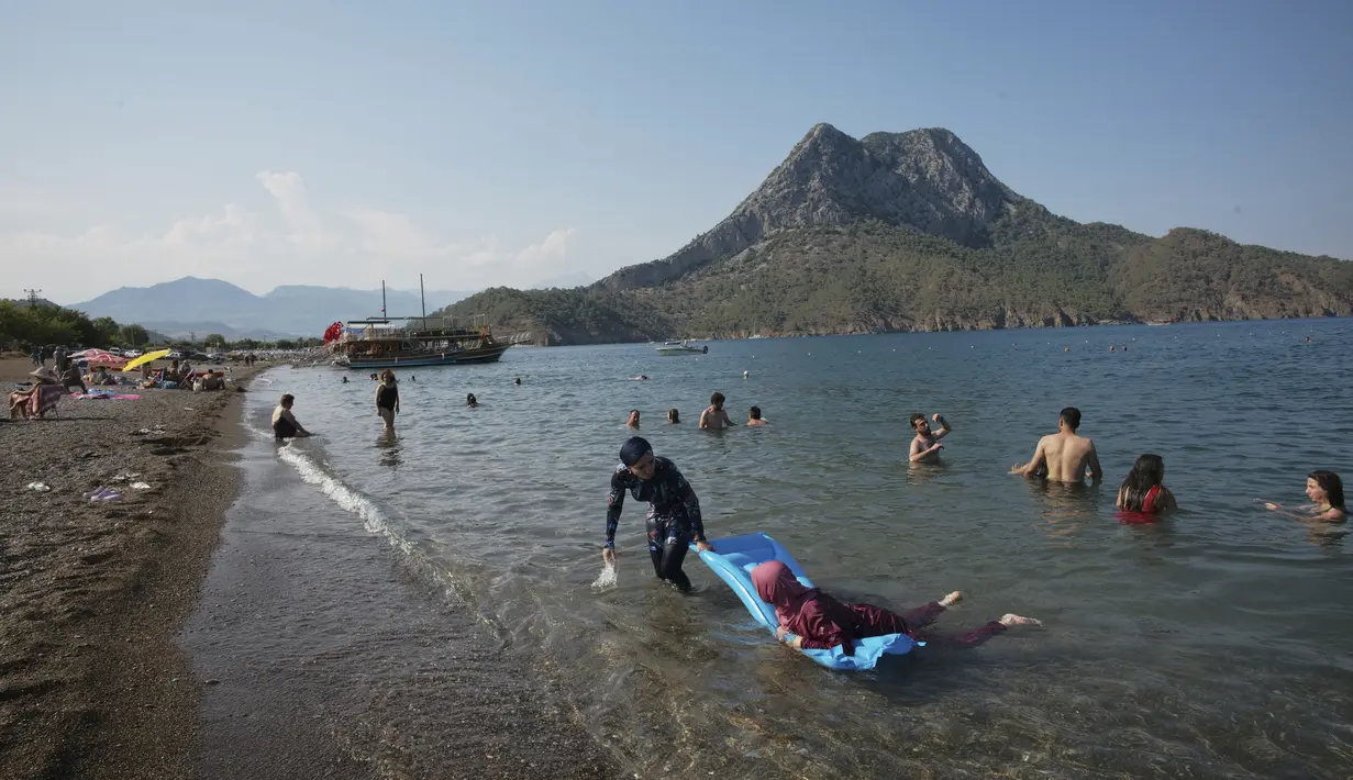 Orang-orang menikmati cuaca cerah, laut dan matahari, sehari sebelum jam malam hari Minggu di Adrasan, 100 kilometer barat Antalya, di Mediterania Turki, Sabtu (19/6/2021).  (AP Photo/Burhan Ozbilici)