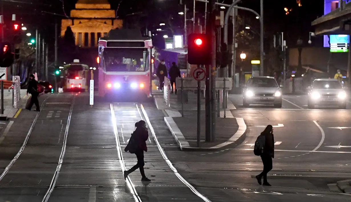 Para komuter menyeberang jalan selama aturan jam malam di Melbourne, pada Selasa (17/8/2021). Kota terbesar kedua di Australia itu memberlakukan pembatasan tinggal di rumah pada pukul 9 malam hingga 5 pagi untuK meredam lonjakan Covid-19 varian Delta. (William WEST/AFP)