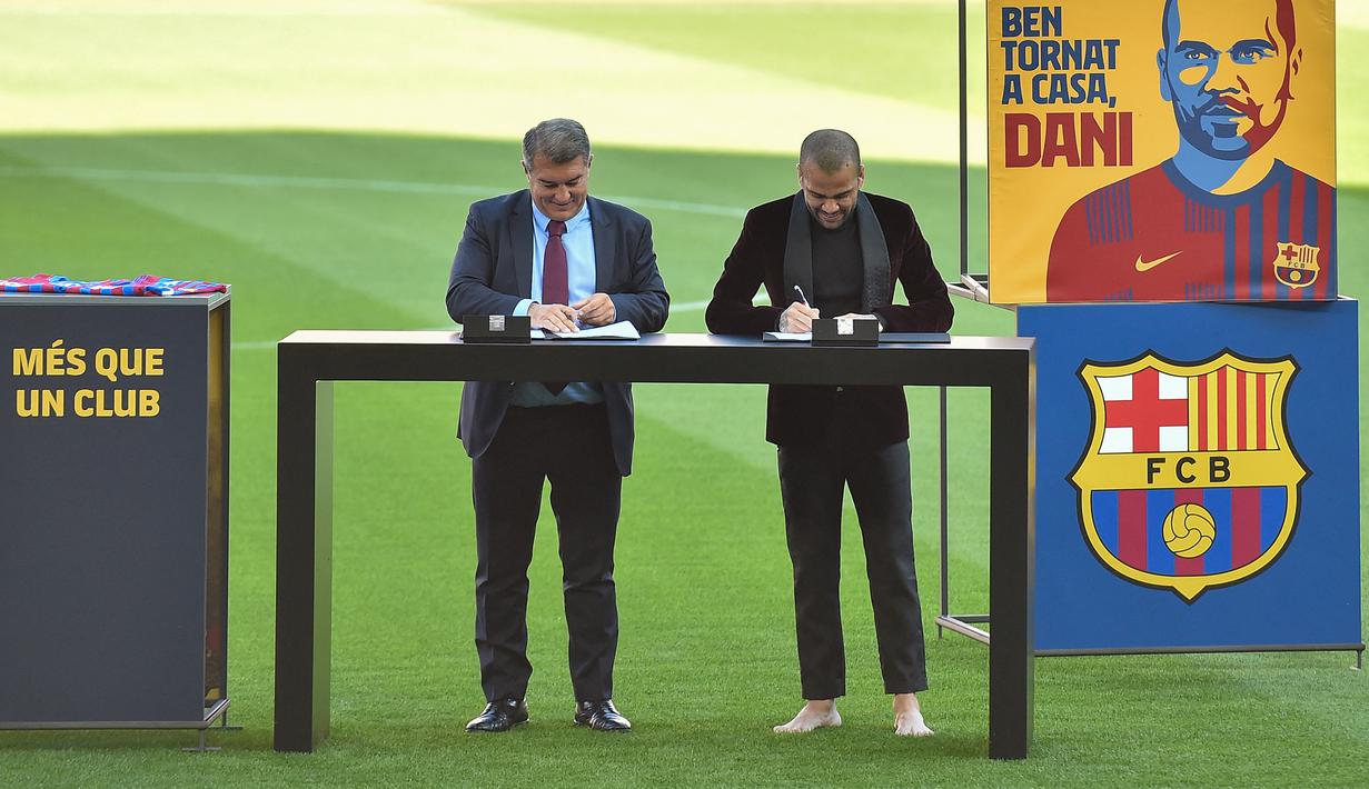 Tak sampai di situ, ketika memasuki lapangan, Dani Alves malah melepas sendal jepitnya alias nyeker. Bahkan hal tersebut bertahan hingga momen teken kontrak di tengah lapangan bersama Joan Laporta (kiri). (AFP/Pau Barrena)
