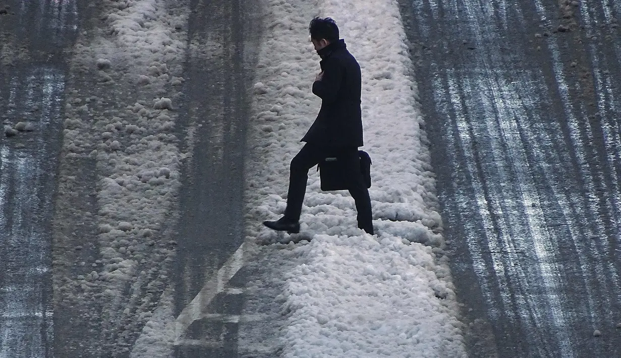 Seorang pria melintasi jalan yang tertutup salju di Tokyo (23/1). Hujan salju membuat keberangkatan penerbangan dan melumpuhkan beberapa layanan kereta api di kota tersebut. (AP Photo / Eugene Hoshiko)