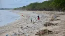 Orang-orang berjalan di antara sampah terdampar di pantai Kuta, Bali, Kamis (31/12/2020). Pantai Kuta tampak sepi menyusul aturan larangan pesta perayaan pergantian tahun baru dan pemberlakuan jam malam untuk pengendalian aktivitas masyarakat yang dibatasi. (SONNY TUMBELAKA / AFP)