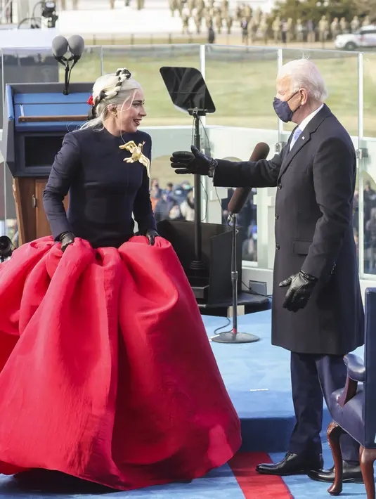 Presiden terpilih AS Joe Biden menyapa penyanyi Lady Gaga saat pelantikannya di Front Barat Capitol AS di Washington, DC (20/1/2021). Joe Biden resmi menjabat sebagai Presiden ke-46 Amerika Serikat. (Jonathan Ernst-Pool/Getty Images/AFP)