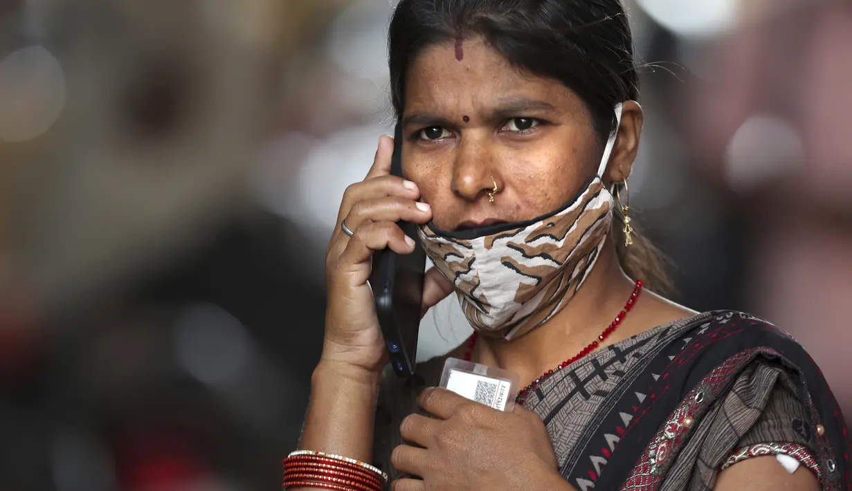 Seorang perempuan berbicara di telepon, maskernya diletakkan di dagu, di pusat vaksinasi di Hyderabad, India, 12 Januari 2022. Wajib pakai masker di India. Dan polisi turun ke jalan, mengawasi orang-orang untuk memastikan mereka ada di tempat.  (AP Photo/Mahesh Kumar A.)
