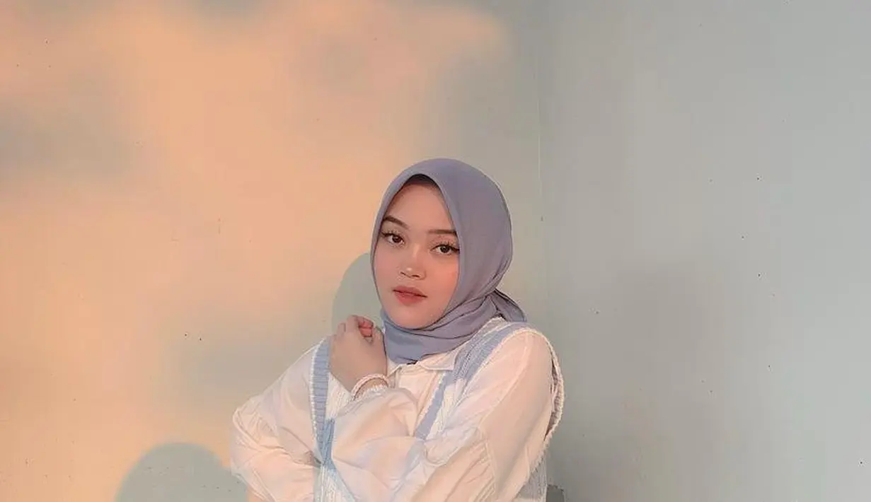 Begini potret adik Rizky Febian memadukan kemeja dengan vest dan celana jeans. Hijab segi empat yang ia kenakan memperlihatkan pipinya yang semakin tirus. (Instagram/putridelinaa).
