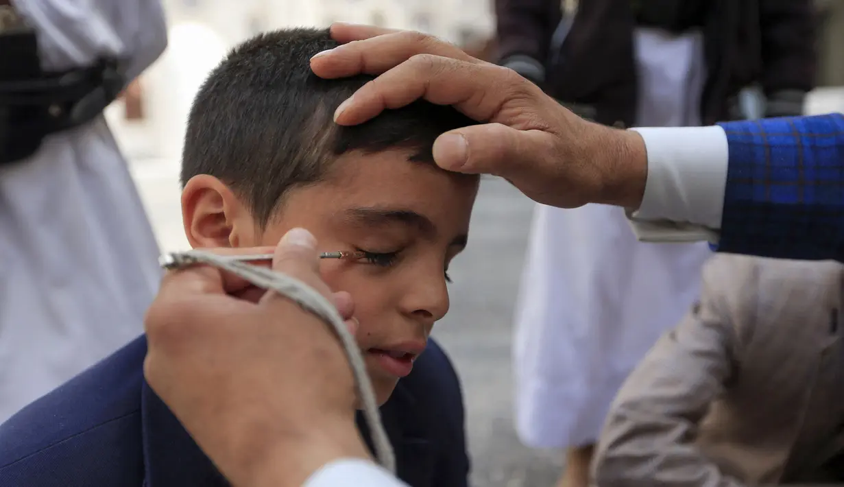 Seorang pria Yaman mengoleskan kosmetik tradisional Kohl ke kelopak mata remaja selama bulan puasa Ramadhan di Masjid Sanaa (16/4/2021).  Umat Muslim di Yaman percaya bahwa kohl atau celak mampu membersihkan dan melindungi mata dari berbagai penyakit. (AFP/ Mohammed Huwais)