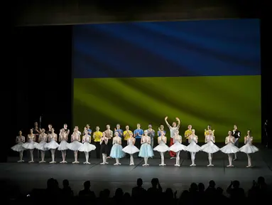 Penari Ukraina dari Balet Kota Kiev menerima tepuk tangan di depan bendera Ukraina yang diproyeksikan ke layar di akhir pertunjukan, di Theater de Chatelet, Paris (8/3/2022). Balet Kota Kiev menari dengan penuh semangat di Paris untuk pertunjukan terakhir dari tur Prancis. (AP Photo/Thibault Camus)