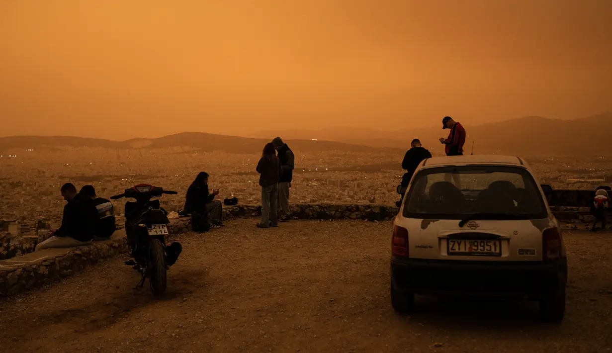 Orang-orang duduk di bukit Tourkovounia menghadap kota Athena, saat angin selatan membawa gelombang debu Sahara ke kota, di Athena, Yunani,Selasa (23/4/2024). (Angelos TZORTZINIS / AFP)