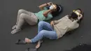 Orang-orang berbaring di tanah saat mereka menggunakan kacamata khusus untuk menyaksikan gerhana matahari hibrida di Jakarta, Kamis (20/4/2023). (AP Photo/Tatan Syuflana)