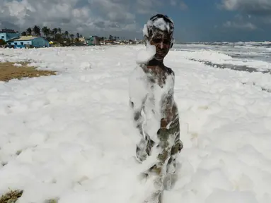 Seorang anak bermain limbah busa yang disebabkan polutan saat bercampur dengan ombak di pantai di Chennai (29/11/2019). Limbah mencapai laut melalui sungai, memicu busa beracun di pantai tersebut. (AFP/Arun Sankar)