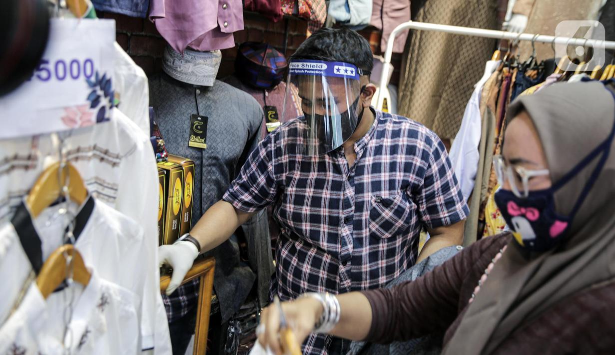 Pedagang menggunakan alat pelindung wajah (Face Shield) saat melayani pembeli di Kawasan Tanah Abang, Jakarta, Senin (18/5/2020). Penggunaan alat pelindung wajah itu sebagai upaya untuk melindungi diri saat berhubungan dengan pembeli dalam pecegahan penyebaran COVID-19. (Liputan6.com/Faizal Fanani)