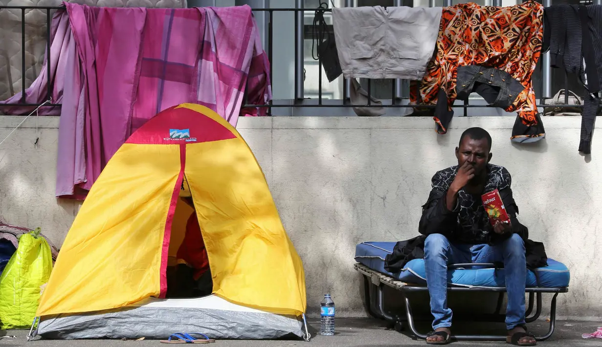 Seorang imigran terlihat menikmati cemilan di sebuah kamp darurat di jalanan Kota Paris, Prancis, Selasa (6/9). Para imigran berkulit hitam tersebut hidup terlantar di pinggir jalan kota tersebut. (REUTERS/Benoit Tessier)