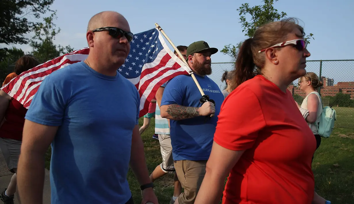 Sejumlah warga berjalan membawa bendera AS saat menggelar aksi solidaritas terkait penembakan di Virginia, AS (14/6). Sebelumnya telah terjadi penembakan terhadap politisi Partai Republik, Steve Scalise saat berlatih bisbol. (Alex Wong/Getty Images/AFP)