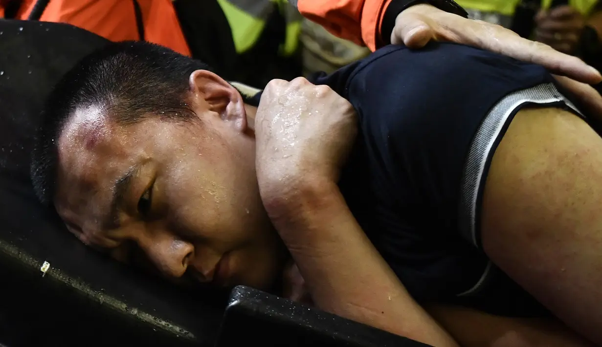 Tim medis membawa seorang pria yang diduga mata-mata China terluka setelah diikat oleh pemrotes pro-demokrasi saat unjuk rasa di bandara internasional Hong Kong (13/8/2019). Polisi anti huru hara bentrok dengan pengunjuk rasa pro-demokrasi di bandara Hong Kong Selasa malam. (AFP Photo/Anthony Wallac