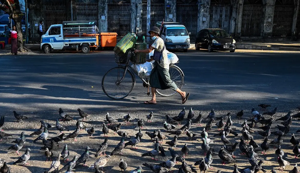 Seorang pria mendorong sepedanya melewati merpati sehari setelah militer Myanmar merebut kekuasaan, Yangon, Myanmar, Selasa (2/2/2021). Militer Myanmar menahan pemimpin yang terpilih secara demokratis Aung San Suu Kyi dan memberlakukan keadaan darurat satu tahun. (STR/AFP)
