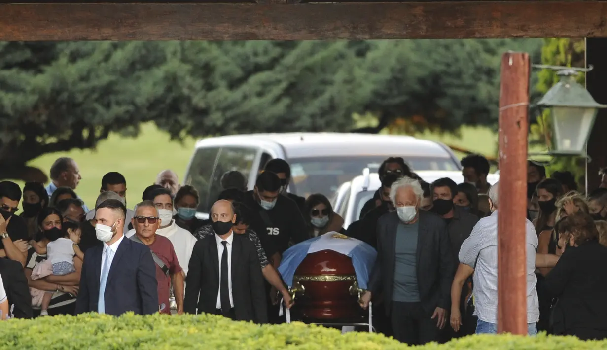 Kerabat dan teman menguburkan jenazah legenda sepak bola Argentina, Diego Maradona sementara polisi menjaga penggemar di luar pemakaman Jardin de Bellavista di Buenos Aires, Kamis (26/11/2020). Maradona meninggal dunia dalam usia 60 tahun pada Rabu (25/11) karena serangan jantung. (AP/Rodrigo Abd)
