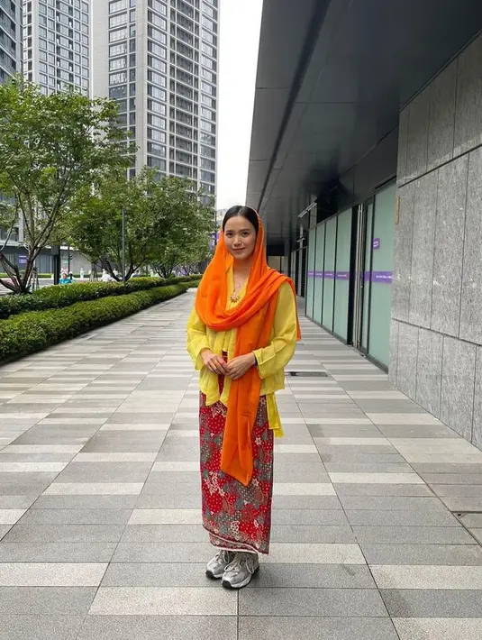 Kebaya dipadukan kerudung oranye serta kain batik merah sebagai bawahannya. Nadhira memadukan outfit tersebut dengan sneakers warna silver. [@indonesianationalwushuteam]