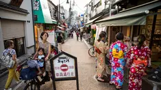 Seorang wanita mengendarai sepeda membawa anak-anaknya melihat ke arah sejumlah wanita yang mengenakan pakaian tradisional yang berbelanja di jalan Yanaka ginza di pusat Tokyo (30/9/2019). Wilayah Yanaka di ibukota Jepang dikenal sebagai salah satu yang paling kuno dan unik. (AFP Photo/Odd Andersen)