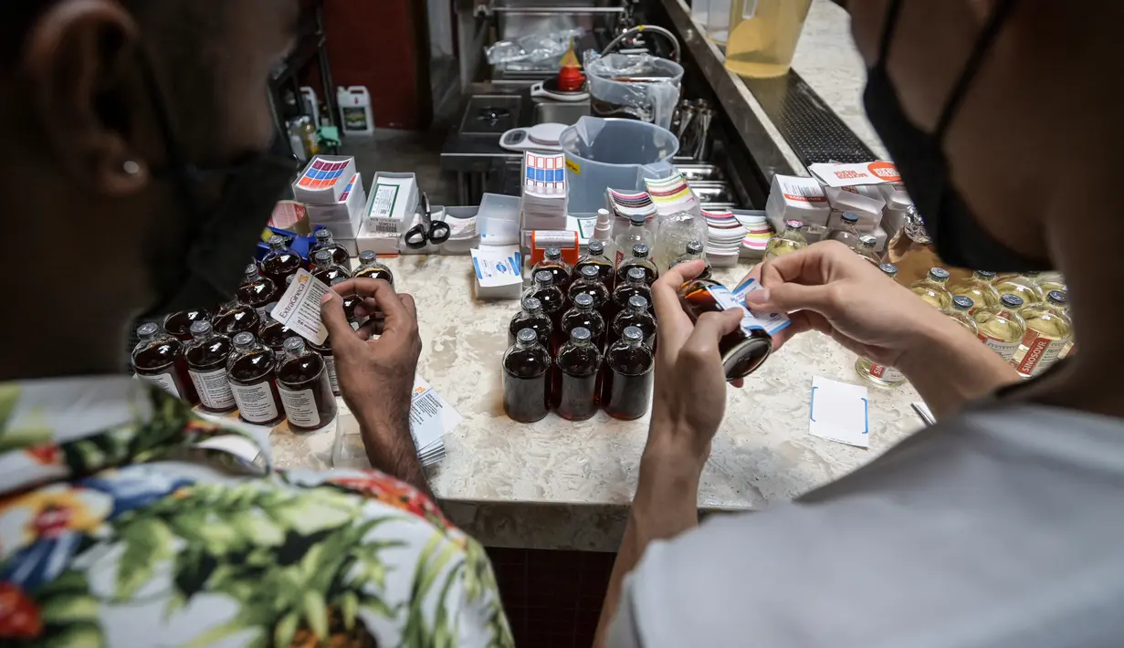 Karyawan memasang label untuk ExtraGineca (kiri) dan minuman Pfizermeister, minuman yang terinspirasi oleh vaksin virus corona Covid-19, di sebuah bar koktail di George Town di pulau Penang, Malaysia (8/9/2021). (AFP/Mohd Rasfan)