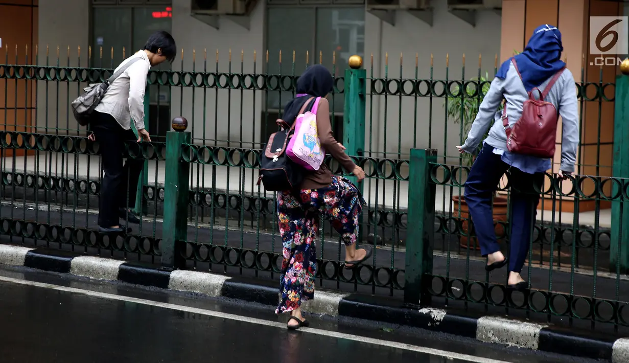 Sejumlah wanita memanjat pagar pembatas di Stasiun Cikini, Jakarta, Rabu, (20/12). Banyaknya penumpang yang mencari jalan pintas dengan melompat pagar untuk menuju akses pintu keluar menyebabkan kemacetan di kawasan stasiun. (Liputan6.com/Johan Tallo)