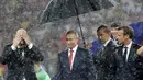 Presiden Rusia, Vladimir Putin dilindungi payung sementara Presiden FIFA Gianni Infantino dan Presiden Prancis Emmanuel Macron basah kuyup saat hujan turun selama penyerahan trofi Piala Dunia 2018 di Stadion Luzhniki, Minggu (15/7). (AP/Matthias Schrader)