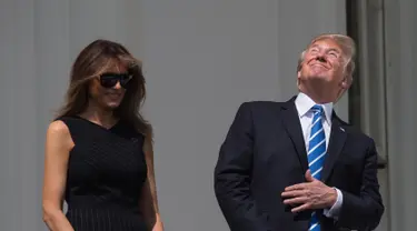 Presiden AS Donald Trump bersama Ibu Negara, Melania Trump menyaksikan  gerhana matahari dari balkon Gedung Putih di Washington, Senin (21/8). Trump tertangkap kamera menyaksikan fenonema langka tersebut tanpa kacamata pelindung. (NICHOLAS KAMM/AFP)