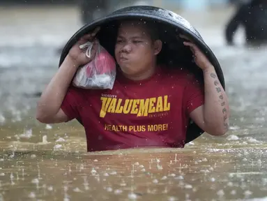 Seorang warga menggunakan bak cucian untuk melindunginya dari hujan saat ia menyeberangi jalan yang banjir akibat Badai Tropis Yagi, yang secara lokal disebut Enteng, di Cainta, provinsi Rizal, Filipina, Senin (2/9/2024). (AP Photo/Aaron Favila)