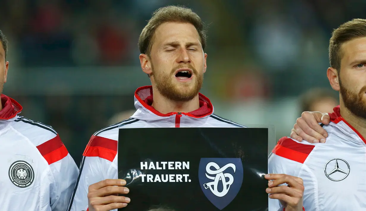 Bek Jerman,  Benedikt Hoewedes memegang tulisan ucapan turut berbelasungkawa kepada para korban jatuhnya pesawat Germanwings di Pegunungan Alpen di Stadion Fritz-Walter, Kamis (26/3/2015). Jerman bermain Imbang 2-2 atas Australia. (REUTERS/Ralph Orlowski)