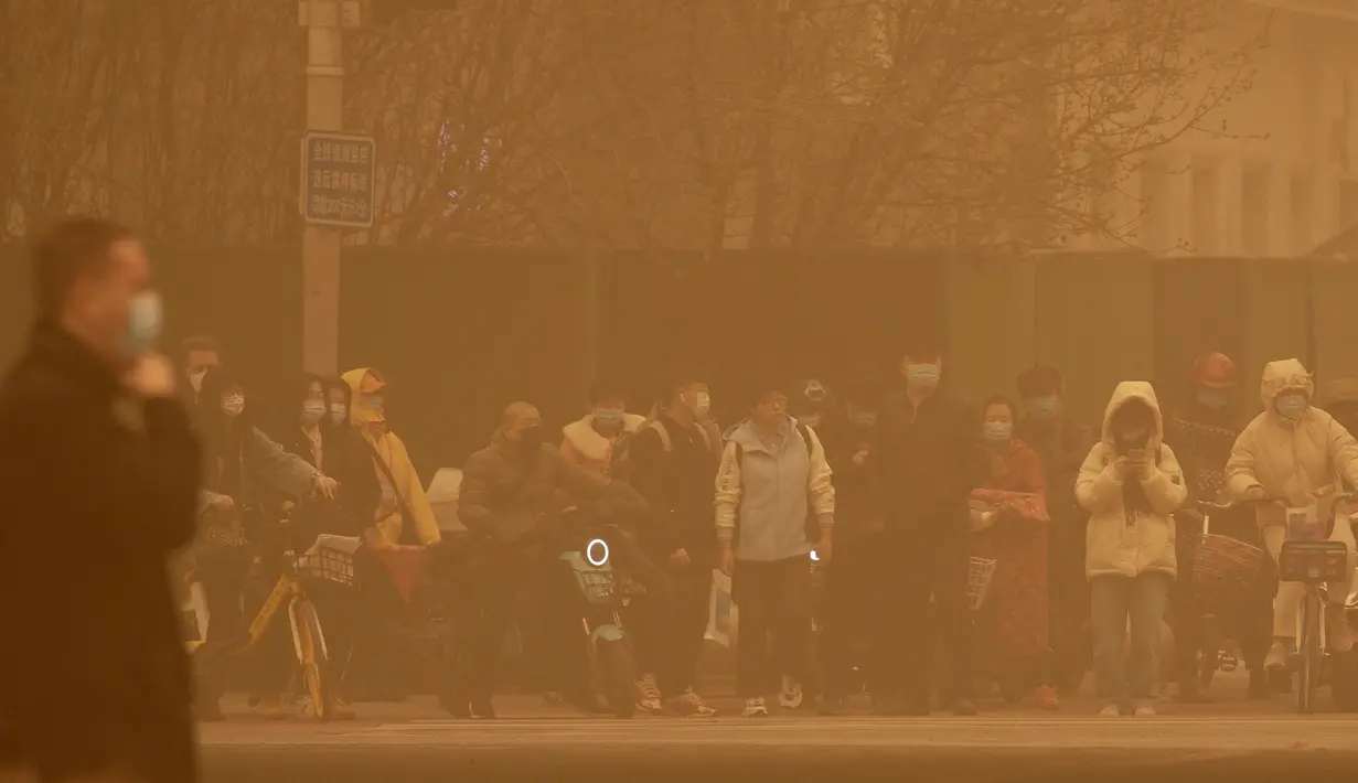 Orang-orang menunggu untuk menyeberangi persimpangan di tengah badai pasir pada jam sibuk pagi hari di Beijing, Senin (15/3/2021). Badai pasir mengubah langit menjadi kuning, membatasi jarak pandang hingga kurang dari 1.000 meter dan mengganggu lalu lintas. (AP Photo/Mark Schiefelbein)