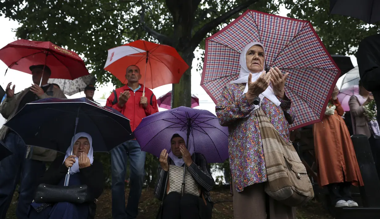 Pria dan wanita berdoa di sebelah truk yang membawa 50 peti mati berisi sisa-sisa korban genosida Srebrenica 1995 di Visoko, Bosnia, 8 Juli 2022. Sebanyak 50 jenazah korban genosida Srebrenica yang baru diidentifikasi akan diangkut ke Memorial Center di Potocari di mana mereka akan dimakamkan pada 11 Juli. (AP Photo/Armin Durgut)