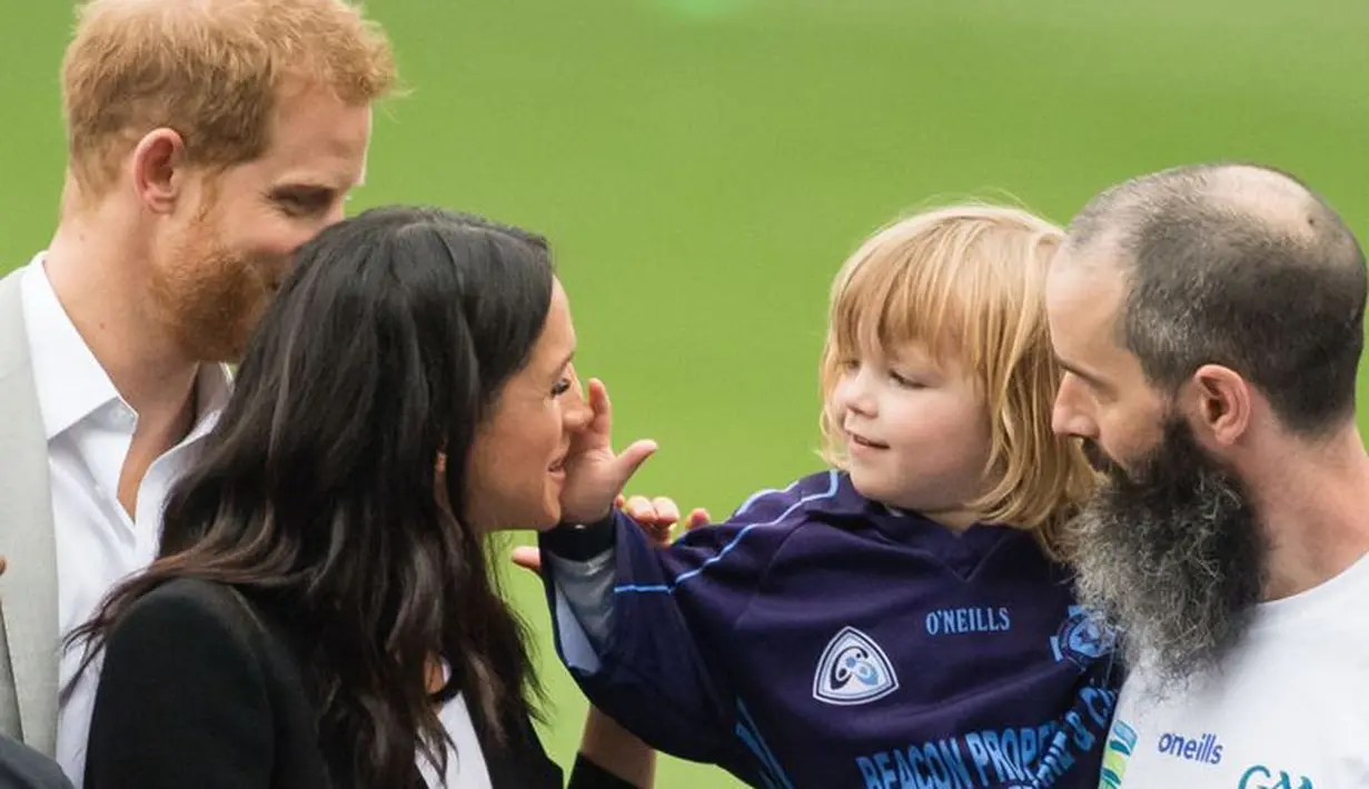 Anak kecil itu terlihat ingin memegang Meghan Markle bahkan menepuk pundaknya untuk mendapatkan perhatian. (Getty Images/Cosmopolitan)