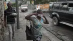 Seorang wanita berjalan melewati pihak berwenang setempat yang memindahkan jenazah pria yang dibakar massa di Port-au-Prince, Haiti, Selasa (25/4/2023). (AP Photo/Odelyn Joseph)