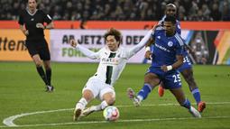 Pemain Borussia Monchengladbach, Kou Itakura (kiri) berebut bola dengan pemain Schalke, Moritz Jenz dalam laga Bundesliga 2022/2023 di Borussia-Park, Monchengladbach (4/2/2023). Pemain yang sejak awal musim 2022/2023 membela Borussia Monchengladbach setelah didatangkan dari Manchester City ini kini memiliki nilai pasar senilai 12 juta euro atau setara Rp195 miliar. (dpa via AP Photo/Federico Gambarini)
