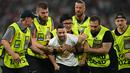 Segerombolan petugas keamanan, yang duduk di pinggir lapangan, kemudian berlari masuk lapangan untuk mengawal supporter itu pergi. (Fabrice COFFRINI / AFP)