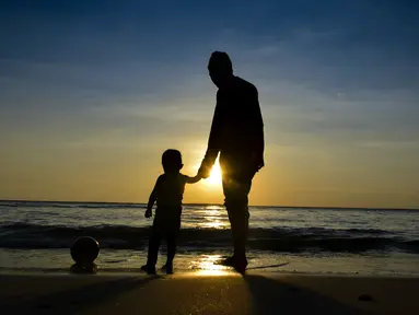 Seorang pria bermain dengan anaknya saat termatahari terbenam terakhir tahun 2019 di pantai Lhoknga provinsi Aceh (31/12/2019). (AFP Photo/Chaideer Mahyuddin)